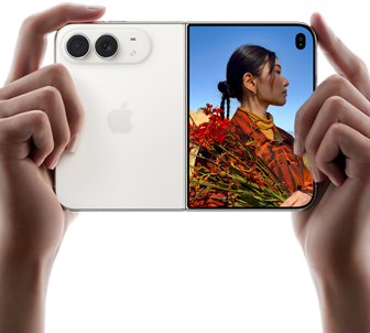 iPhone Duo, Star White colour, held by two hands in horizontal orientation, unfolded, left panel shows 48MP Dual Fusion rear cameras, right panel shows person getting their picture taken on outer display, the subject of the photo is able to see their face as their picture is getting taken using Duo Preview