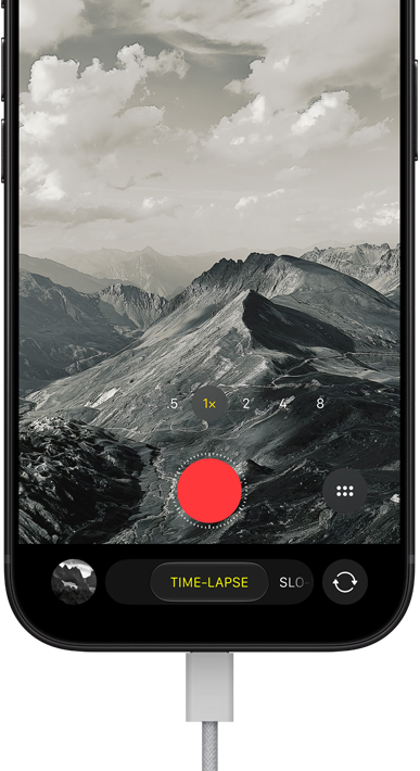 iPhone 18 Pro, front exterior, displaying a mountainous landscape, with the camera mode overlay in Time-Lapse mode, with power cord attached to charging port