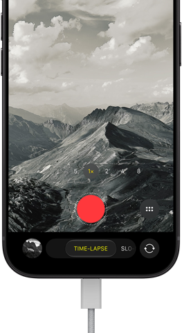iPhone 18 Pro, front exterior, displaying a mountainous landscape, with the camera mode overlay in Time-Lapse mode, with power cord attached to charging port