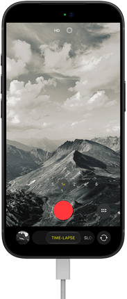 iPhone 18 Pro, front exterior, displaying a mountainous landscape, with the camera mode overlay in Time-Lapse mode, with power cord attached to charging port